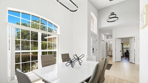 A spacious room with a large white table, multiple chairs, and a view of greenery outside.