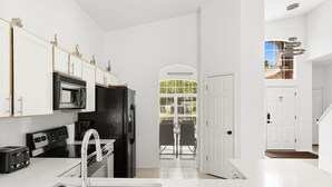 A modern kitchen with white cabinetry, a black refrigerator, a built-in microwave, a stainless steel range hood, and a black countertop.