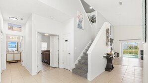 A spacious, well-lit interior with a staircase leading to a second floor, a kitchen area, and a view of a swimming pool.