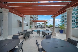 Une terrasse extérieure avec des tables et des chaises, une piscine et une vue sur l’océan.