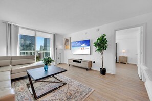 A modern living room with a sofa, coffee table, TV, and a balcony with city views.