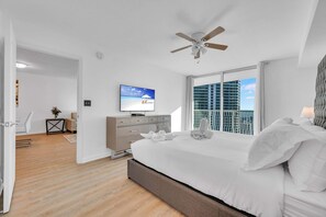 Une chambre d’hôtel avec un lit, une télévision, un ventilateur de plafond et une vue sur un immeuble par la fenêtre.