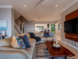 A modern living room with a sectional sofa, a wooden coffee table, and a television mounted on the wall. - Beach Blessing - 180° Sea Views (KwaDukuza)