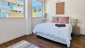 Ein Schlafzimmer mit einem großen Bett, Blick auf benachbarte Gebäude und einem Deckenventilator.