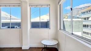Ein Eckzimmer mit großen Fenstern, einem kleinen runden Tisch und Holzdielen.
