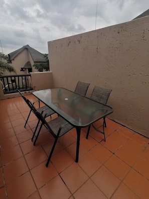 Una mesa con cubierta de vidrio y cuatro sillas en un patio con baldosas.