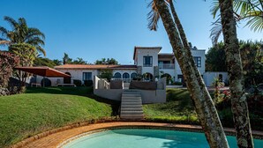 A swimming pool with a brick border, a clear blue pool, and a house with a red roof in the background. - Sea Vista - Awesome Sea Views (uMhlanga)