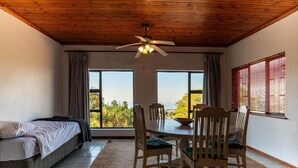 A room with a bed, a dining table with chairs, a ceiling fan, and large windows with curtains. - Sea Vista - Awesome Sea Views (uMhlanga)