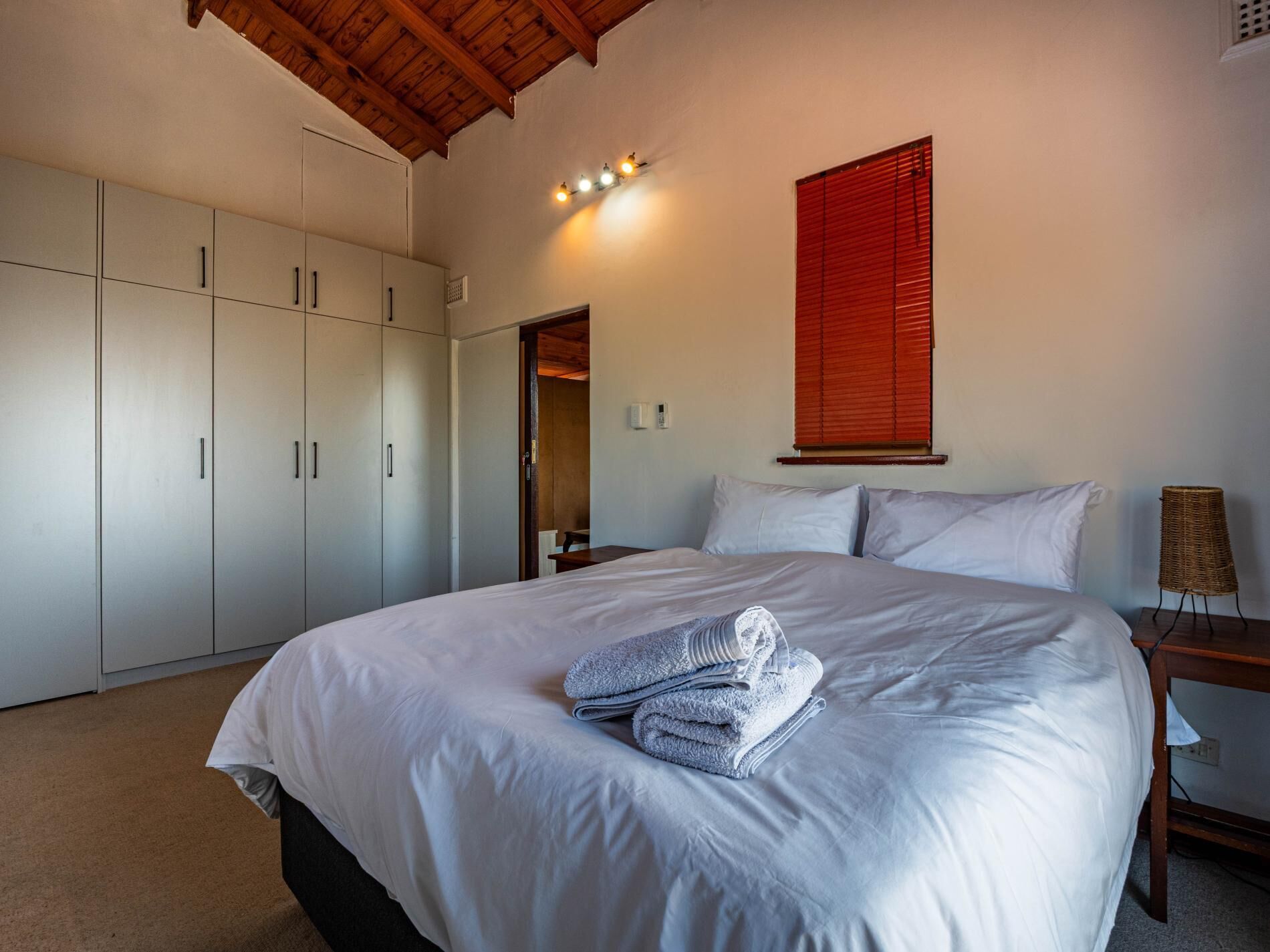 Une chambre à coucher avec un grand lit, une armoire, une table de chevet, une lampe et une fenêtre avec des stores.