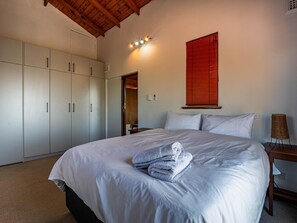 Un dormitorio con una cama grande, un armario, una mesita de noche, una lámpara y una ventana con persianas.