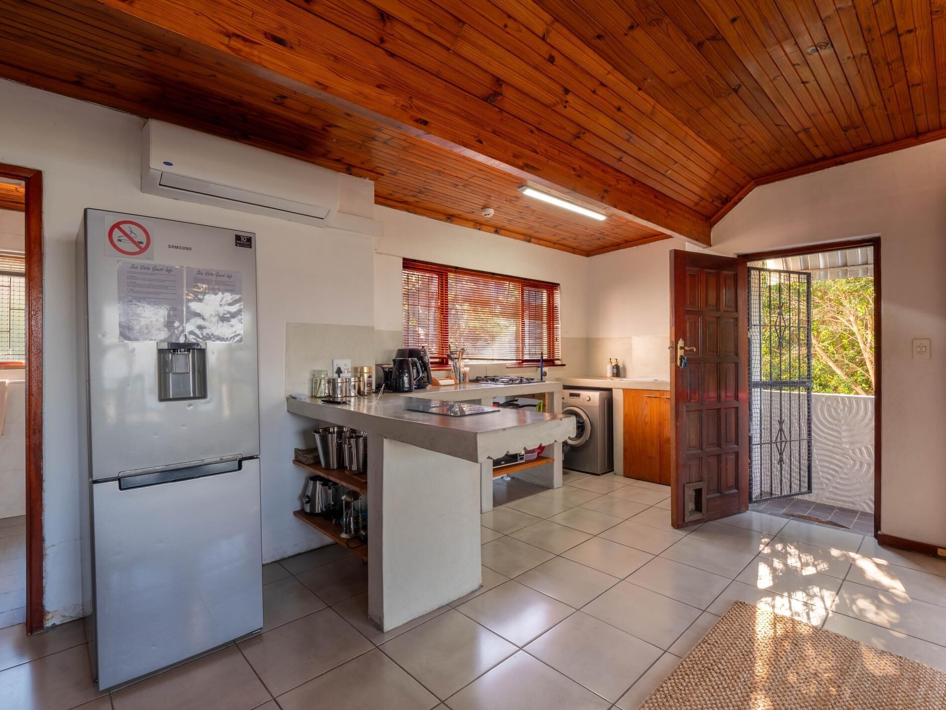 A compact kitchen with a built-in refrigerator, a washing machine, and a wooden ceiling.