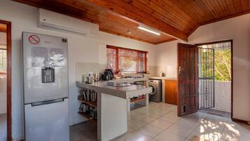 A compact kitchen with a built-in refrigerator, a washing machine, and a wooden ceiling.