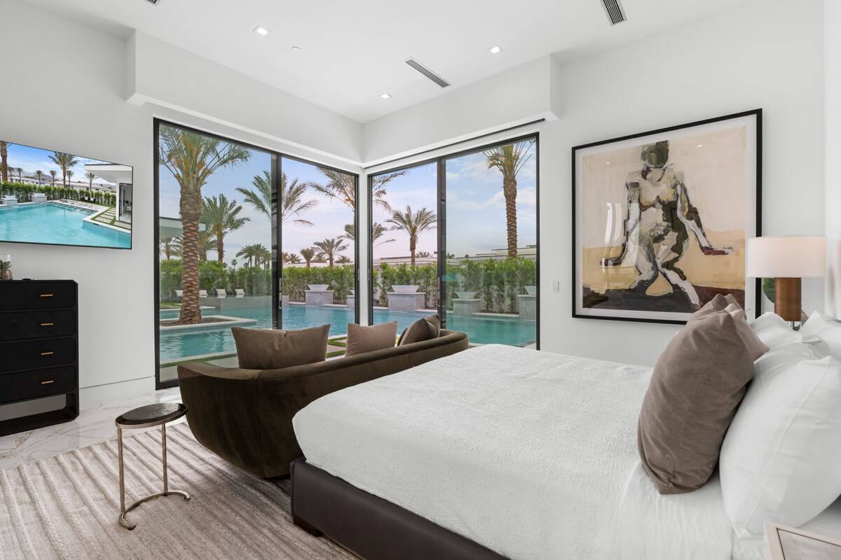 Een moderne slaapkamer met een groot bed, uitzicht op een zwembad en een schilderij aan de muur.