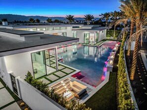 Una casa moderna con una amplia piscina, paredes de cristal y un jardín bien cuidado.