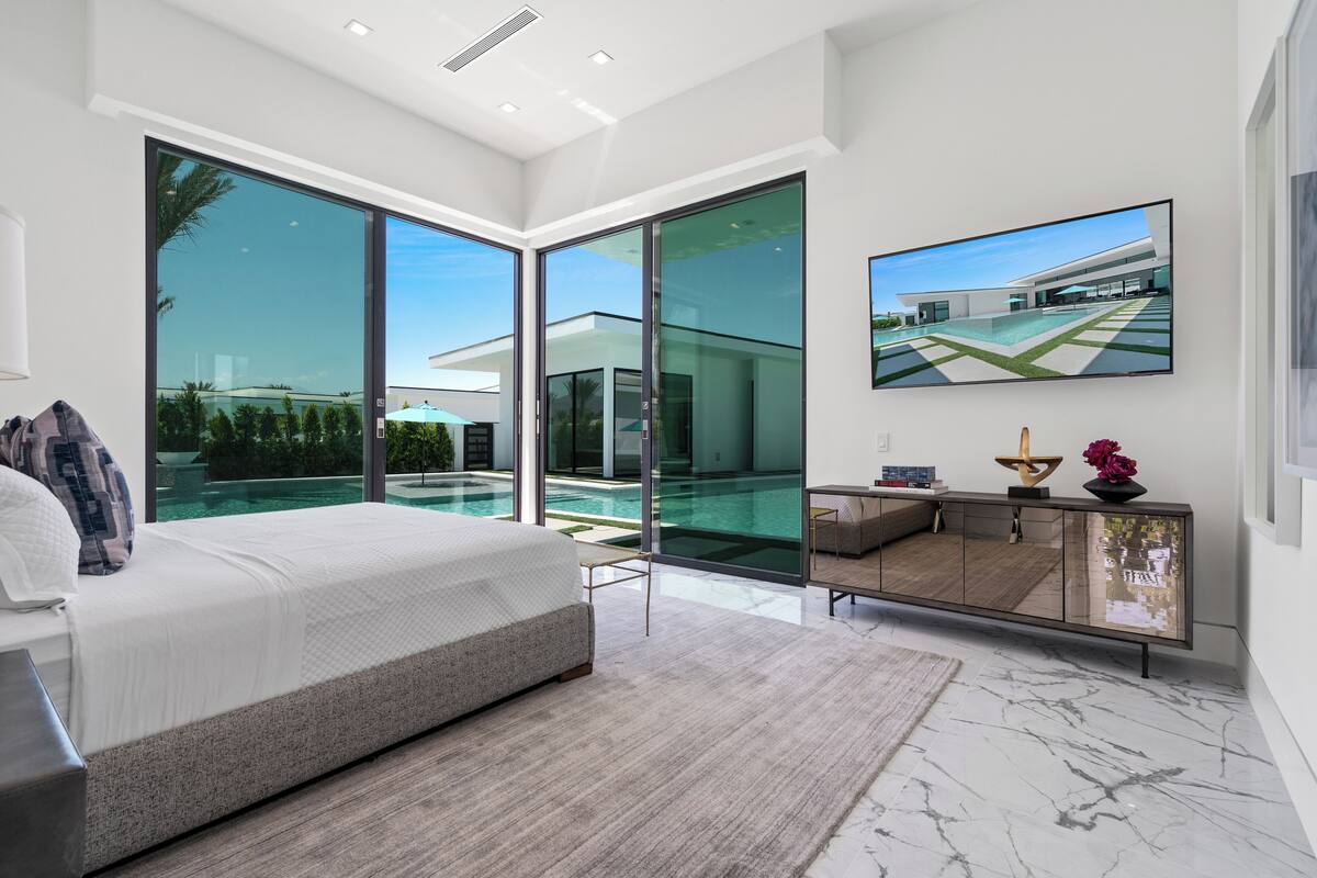 Een moderne slaapkamer met een groot bed, een glazen balkon en uitzicht op een zwembad.