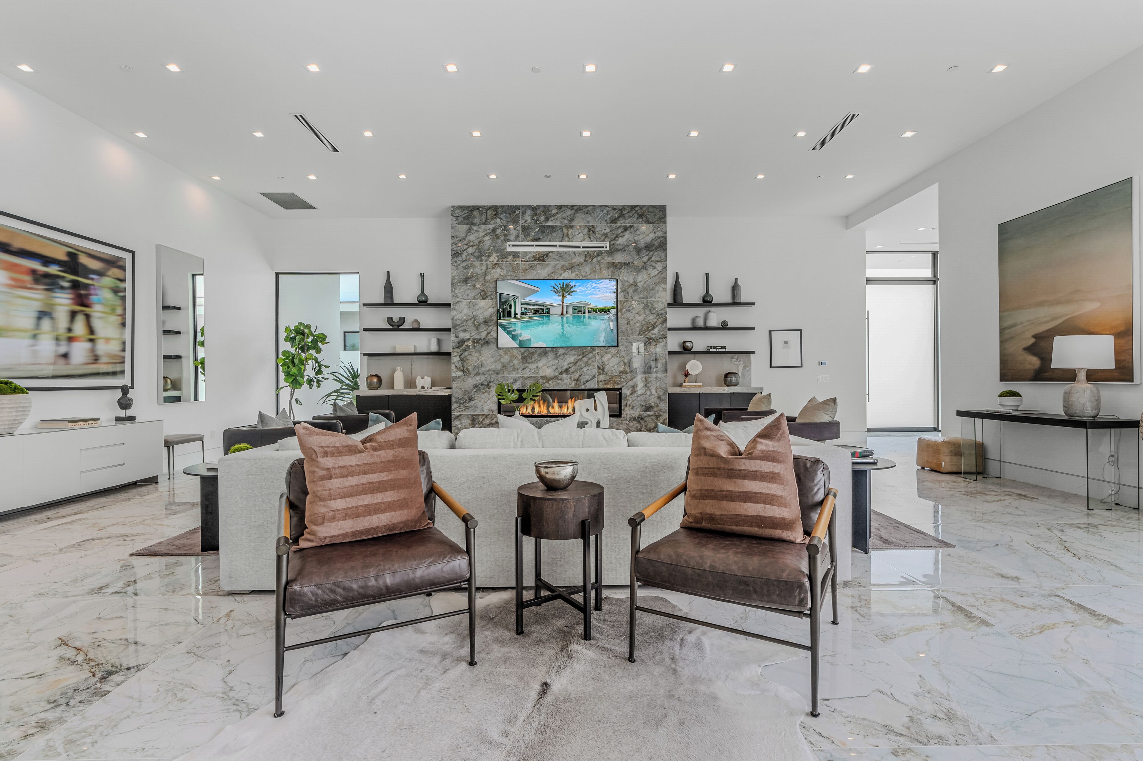 A spacious living room with a large TV, a fireplace, and a marble floor.