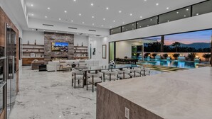 Un interno moderno con pavimento in marmo, angolo bar, zona pranzo e piscina con vista sul tramonto.