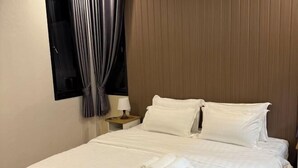 A neatly made bed with white linens and rolled towels, a wooden nightstand with a lamp, and a window with curtains. - Big Elephant Hotel (Yasothon)