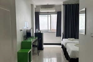 Una camera d'albergo con una scrivania, due letti, una finestra con tende e un condizionatore d'aria.
