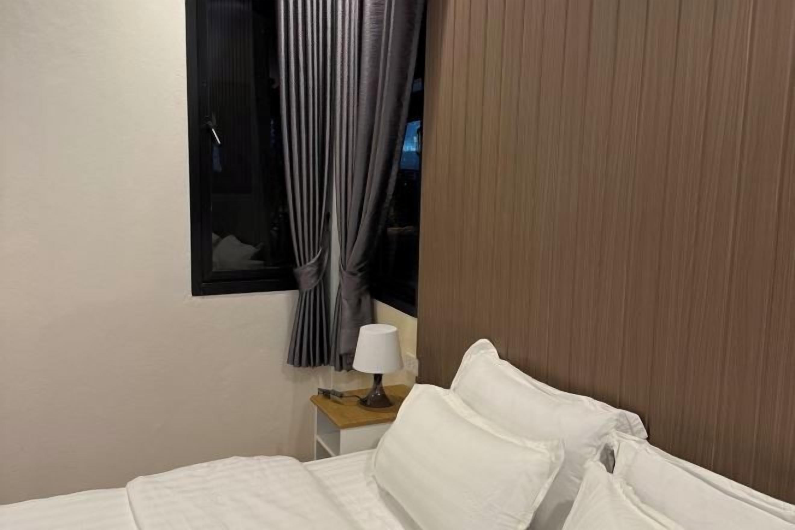 A hotel room with a bed, a nightstand with a lamp, and a window with curtains.