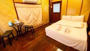 A single bedroom with a bed, a small table, two chairs, an air conditioning unit, and a curtain. - Big Elephant Hotel (Yasothon)