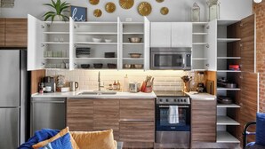 A modern kitchen with white cabinets, a built-in oven, and a microwave. There are decorative plates on the wall and a plant on the counter. - The Bentley Collection - Urban Luxe Loft, Free Valet, Pool & 24/7 Gym (Dallas)
