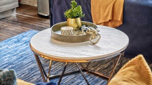 A round coffee table with a metal base, a small potted plant, and decorative items on a blue patterned rug. - The Bentley Collection - Urban Luxe Loft, Free Valet, Pool & 24/7 Gym (Dallas)