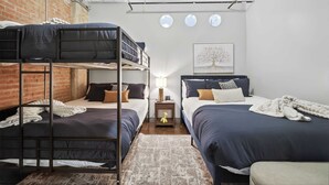 A dormitory room with bunk beds, a small bedside table with a lamp, and a framed artwork on the wall. - The Bentley Collection - Urban Luxe Loft, Free Valet, Pool & 24/7 Gym (Dallas)