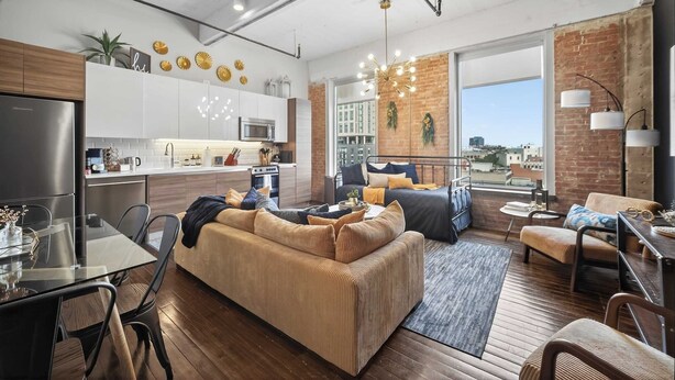 A modern living room with a sofa, dining table, and chairs. There is a kitchen area with cabinets and appliances. The room has large windows and a view of the city. - The Bentley Collection - Urban Luxe Loft, Free Valet, Pool & 24/7 Gym (Dallas)