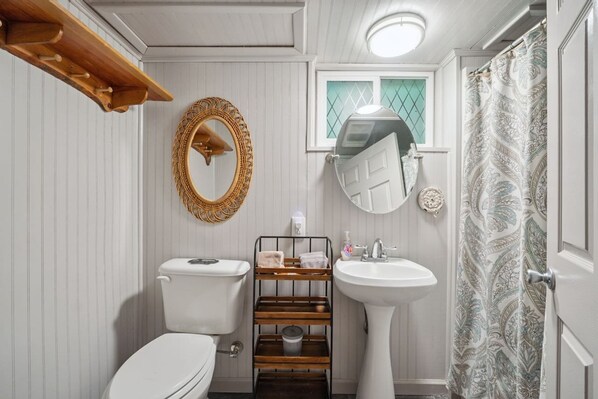 A bathroom with a toilet, a wooden shelf with toiletries, a sink, and a mirror. - Welcoming 4-bedroom cabin near Linville Falls (Newland)