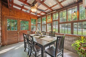 A dining area with a wooden table and chairs, large windows, and a ceiling fan. - Welcoming 4-bedroom cabin near Linville Falls (Newland)