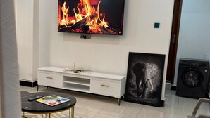 A modern living room with a flat-screen TV mounted on the wall, a white entertainment unit below, a grey sofa, and a framed picture of an elephant.