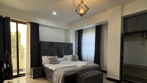 A modern bedroom with a large bed, a small desk, a wardrobe, and a sliding glass door to the outside.