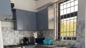 A compact kitchen with grey cabinets, a white marble countertop, a gas stove, a microwave, and a window with a view of trees.