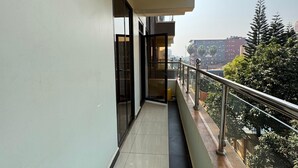 A narrow balcony with a metal railing, a tiled floor, and a view of a cityscape with buildings and trees.