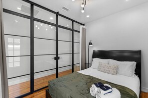 Habitación de hotel con cama, colcha verde, cabecera, mesita de noche, lámpara y puerta corredera de cristal que ofrece vistas al exterior.