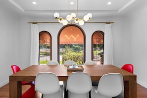 Un comedor con una mesa de madera, sillas blancas y rojas, y vistas a través de ventanas arqueadas.