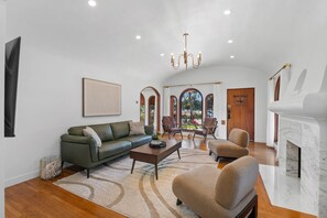 Un salón amplio con un sofá verde, un sillón beige, una mesa de centro de madera y una chimenea.