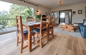 A dining area with a wooden table and chairs, a vase of flowers, and a view of greenery outside. - 3 bedroom nice apartment in Confolens (Confolens)