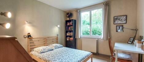 A bedroom with a wooden bed, a desk with a chair, a bookshelf, and a window with curtains.