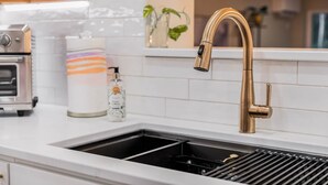 A kitchen with a stainless steel oven, a white tiled backsplash, a gold faucet, and a black sink with a grid drain. - The Luna Lodge - close to old Orchard beach (Saco)