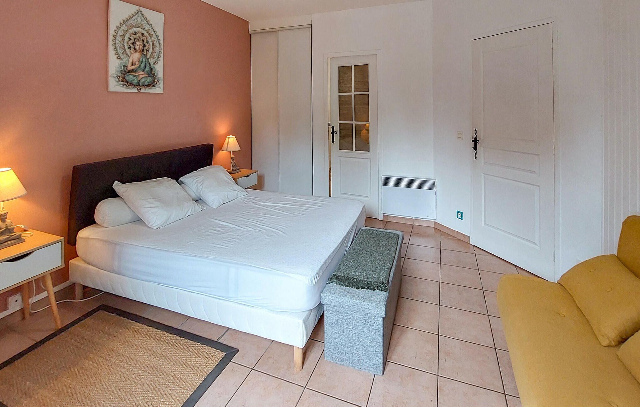 Habitación de hotel con cama, mesita de noche, lámpara, banco y una silla.