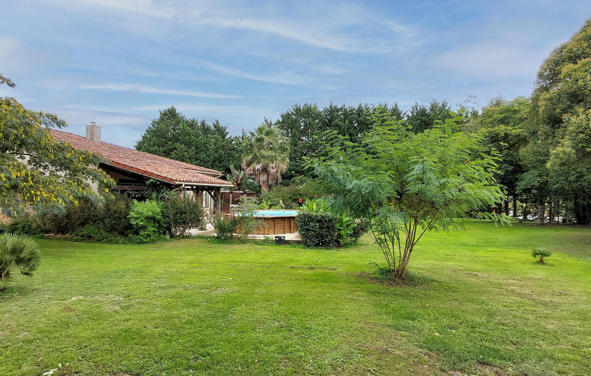 A house with a tiled roof, surrounded by a well-maintained lawn and various trees.