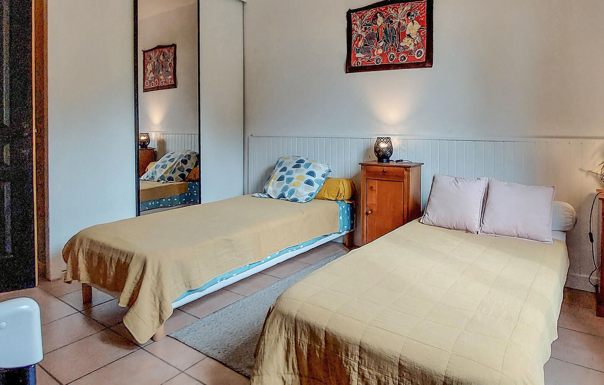 A bedroom with two beds, a wooden nightstand, a mirror, and a wall-mounted picture.