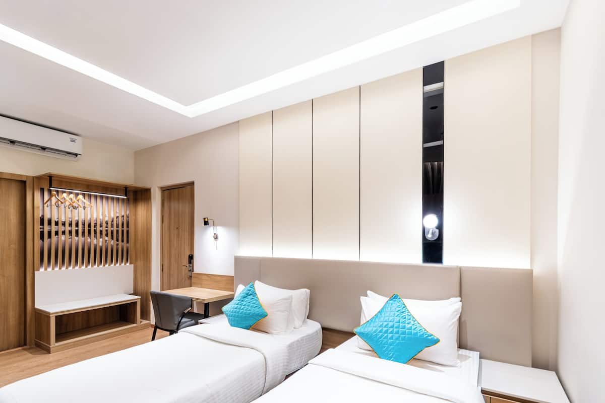 Ein modernes Hotelzimmer mit zwei Betten, einem Schreibtisch und einem Kleiderschrank.