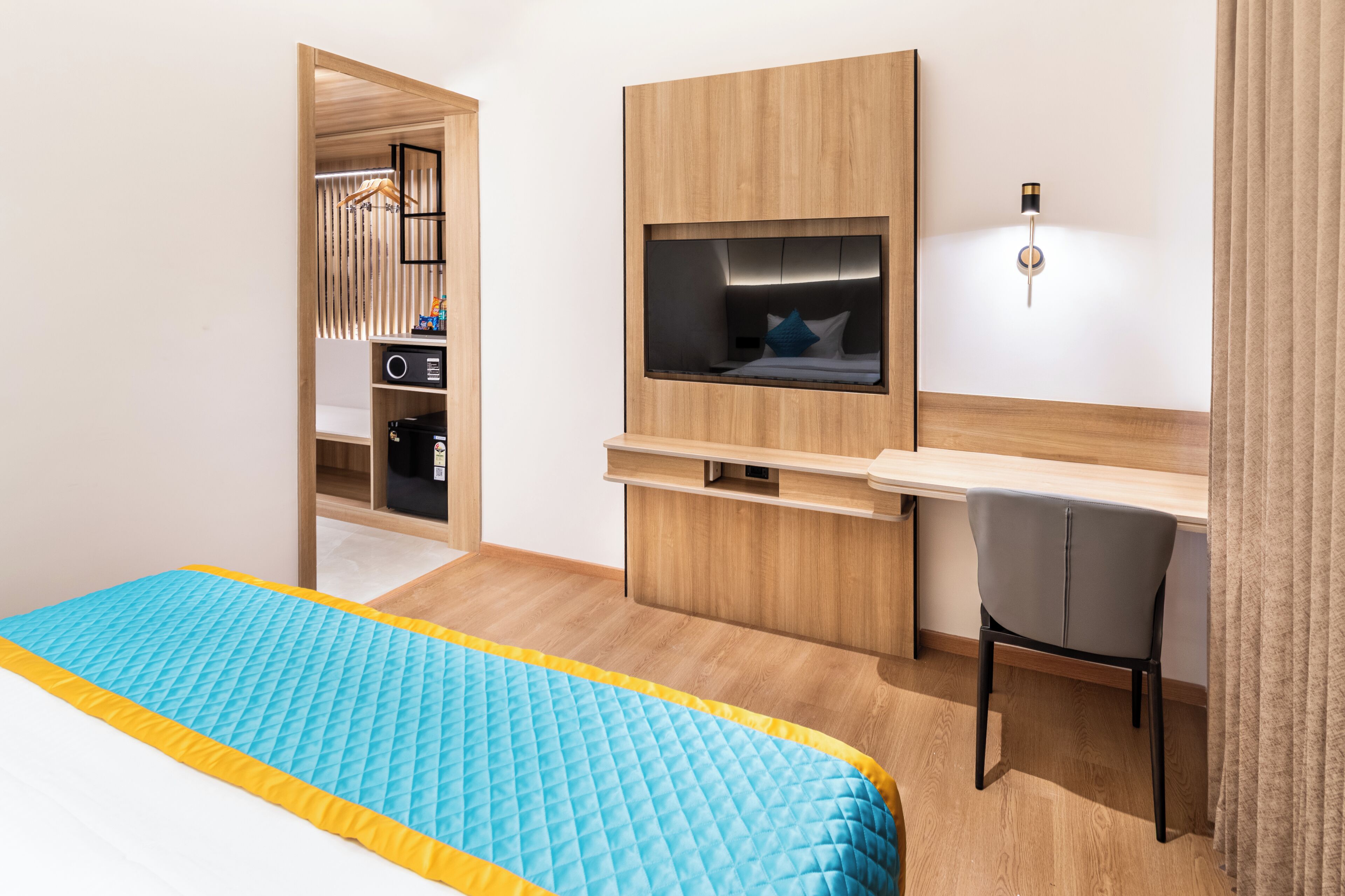 A hotel room with a bed, a desk, a chair, a TV, and a wardrobe.