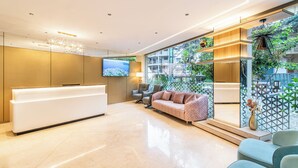 A modern reception area with a white reception desk, a sofa, and a large window with a city view. - Hotel Lenexa By Bestinn Leisure (Bengaluru)