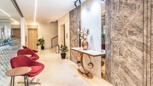 A modern reception area with a marble reception desk, red chairs, and a potted plant. - Hotel Lenexa By Bestinn Leisure (Bengaluru)