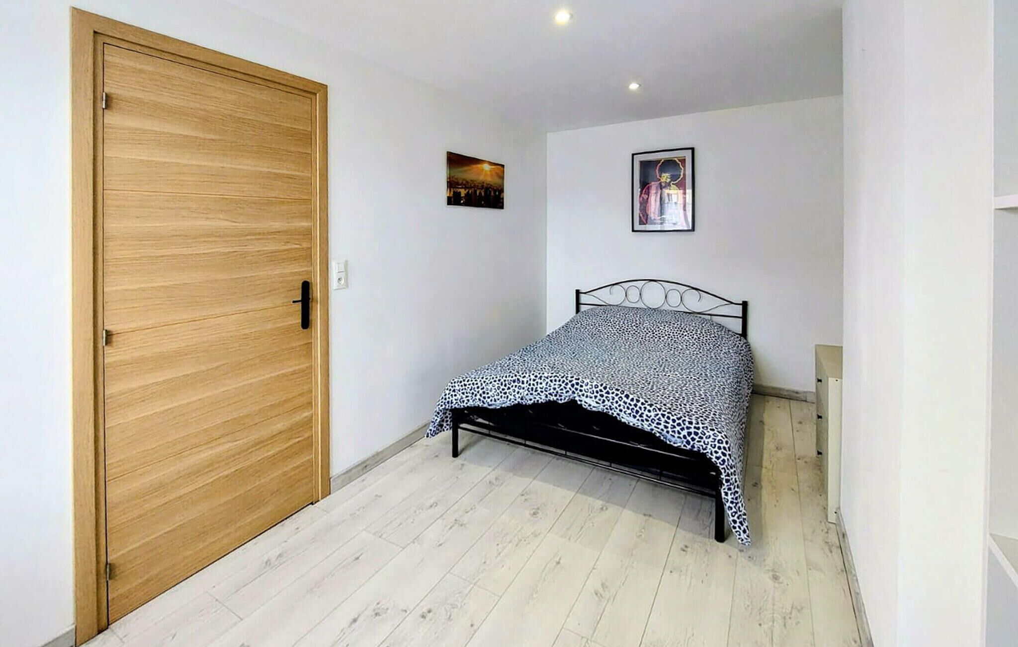 Une chambre avec une porte en bois, un lit recouvert d’une couvre-lit à motifs et deux tableaux encadrés accrochés au mur.