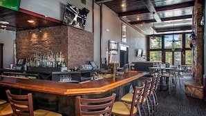 Zona de bar con pared de piedra, mostrador de madera y varios taburetes.